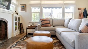 Ein gemütliches Wohnzimmer mit Kamin, einer Couch, Poufs und einem gemusterten Teppich.