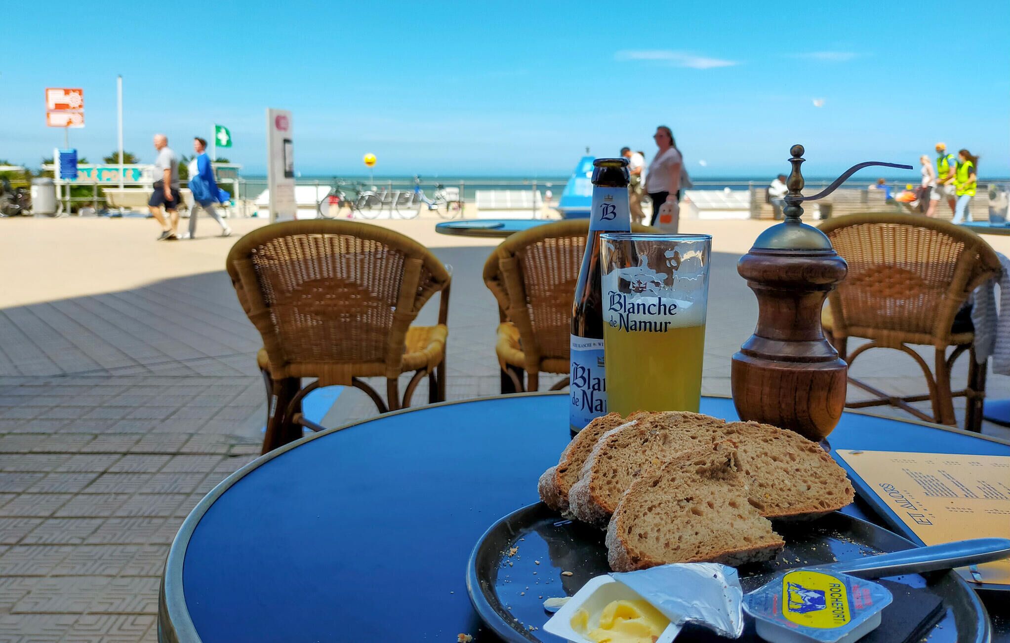 A table with a bottle of Blanche de Narmer, a glass of yellow drink, slices of bread, and a butter dish.