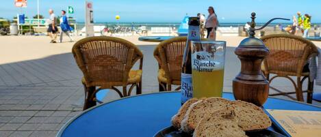 A table with a bottle of Blanche de Narmer, a glass of yellow drink, slices of bread, and a butter dish.