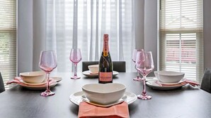 Una mesa de comedor dispuesta con cristalería rosa, cuencos blancos, una botella de champán y una servilleta rosa.