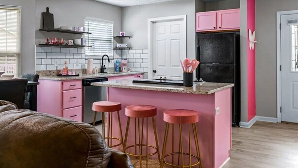 Una cocina moderna con detalles en rosa, un refrigerador negro y una isla central con taburetes.