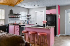 A modern kitchen with pink accents, a black refrigerator, and a central island with stools. - Dolly Parton! Pink! Trolley Route! Fire Pit! Girls Night! Murals! Hottub! (Pigeon Forge)