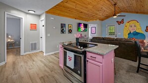 Una cocina con armarios rosados, techo de madera y un mural en la pared.
