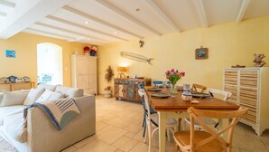 A dining area with a wooden table, chairs, and a vase of flowers. There is a sofa and a cabinet in the background. - Maison au cœur de la Chaume + Garage fermé (Les Sables-d'Olonne)