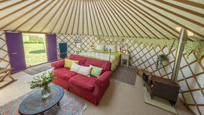 Interior de una yurta con un sofá rojo, una mesita con un jarrón y un estufa de leña.