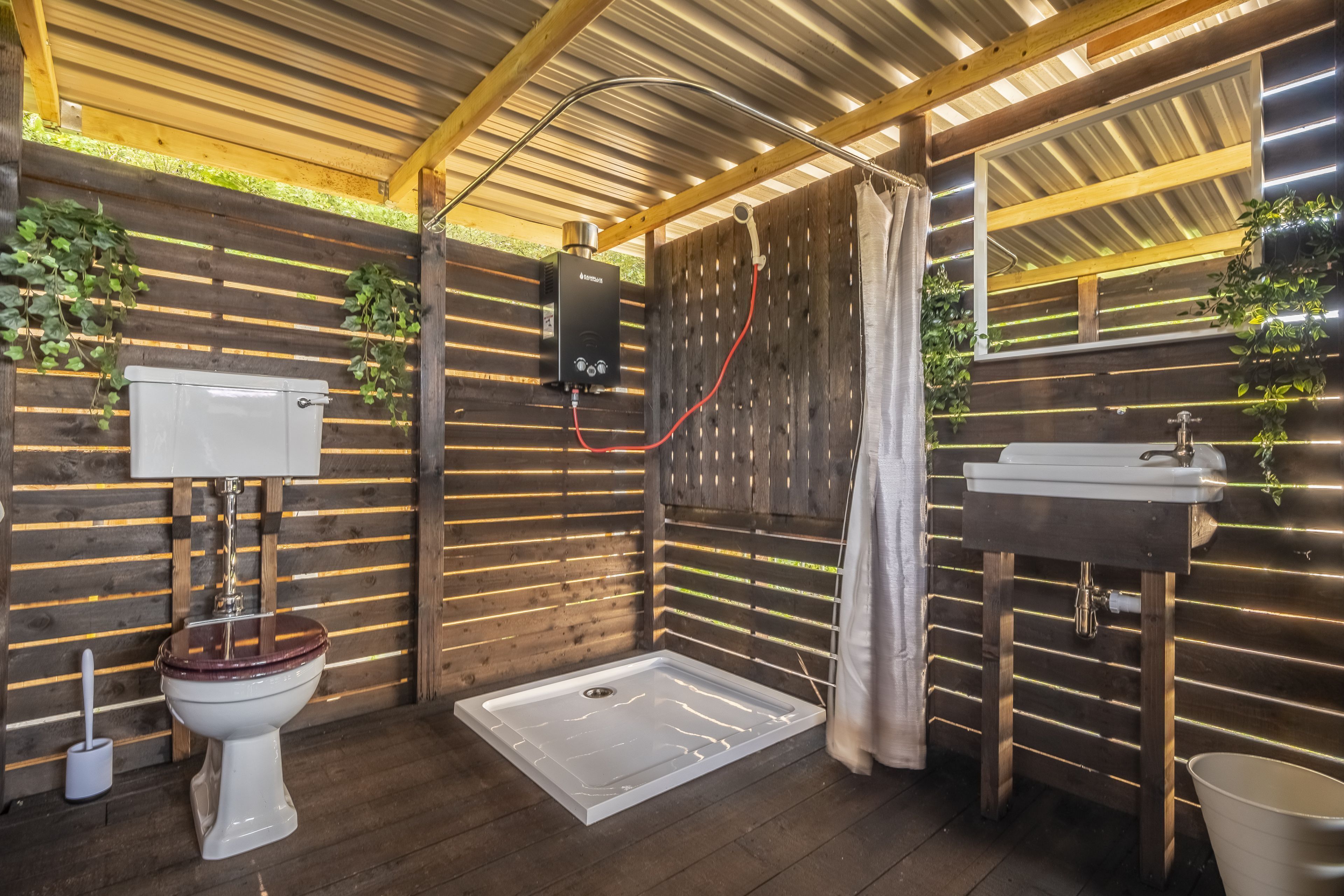A bathroom with a toilet, bidet, shower, and sink, all with wooden paneling and green plants.
