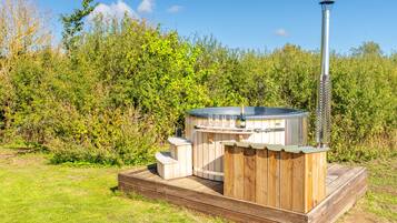 Een hottub met een houten terras en schoorsteen, omgeven door groen.