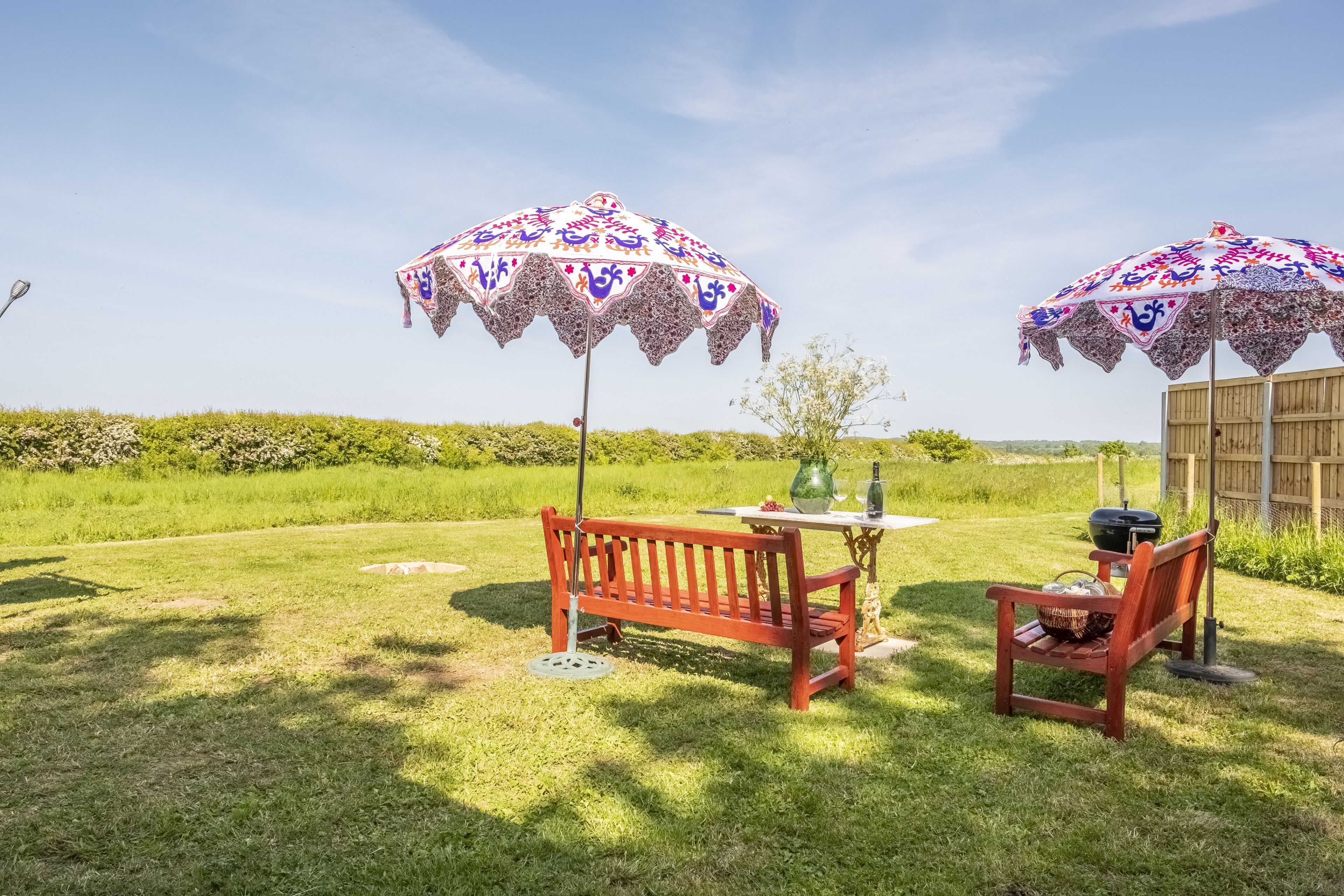 Een terras met twee houten banken, een tafel en twee decoratieve parasols.