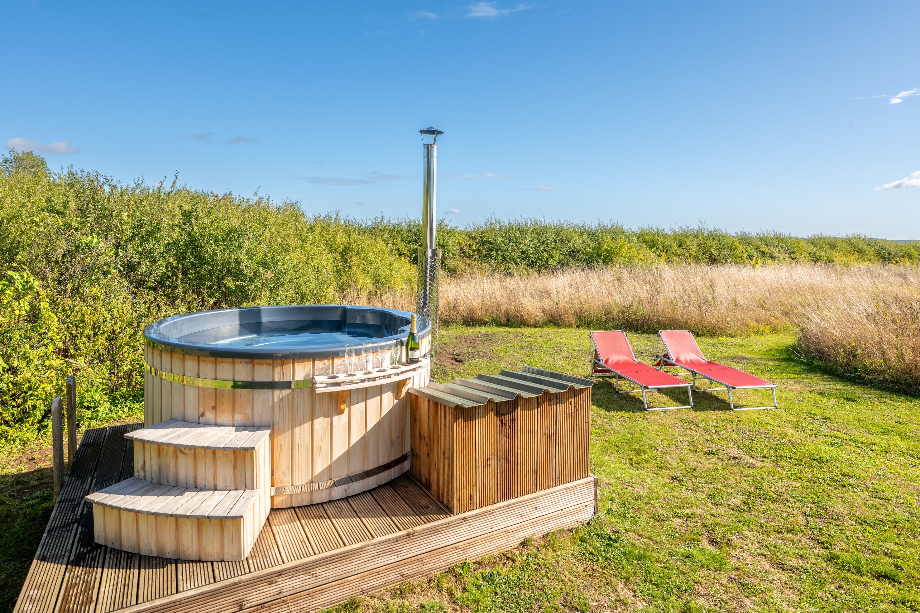 A hot tub with wooden steps and lounge chairs on a deck.