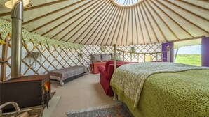 Interior de una yurta con estufa de calefacción central, varias camas y vistas al exterior.