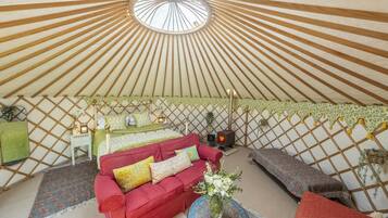 A yurt interior with a red sofa, a green table, and a patterned rug.