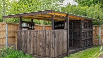 A wooden structure with a covered patio area, a fenced backyard, and a grill setup.