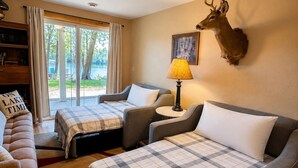 Camera d'albergo con due letti, un divano, una lampada, una testa di cervo appesa al muro e vista sull'esterno.