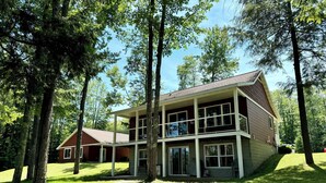 Una casa a due piani con un ampio portico, circondata da alberi e da un prato.