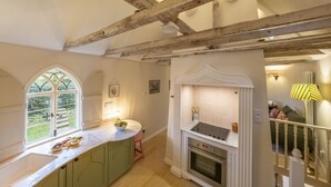 A kitchen with a large window, wooden beams, a white countertop, and a built-in oven. - A fairy-tale luxurious cottage - The Tea Caddy (Colchester)