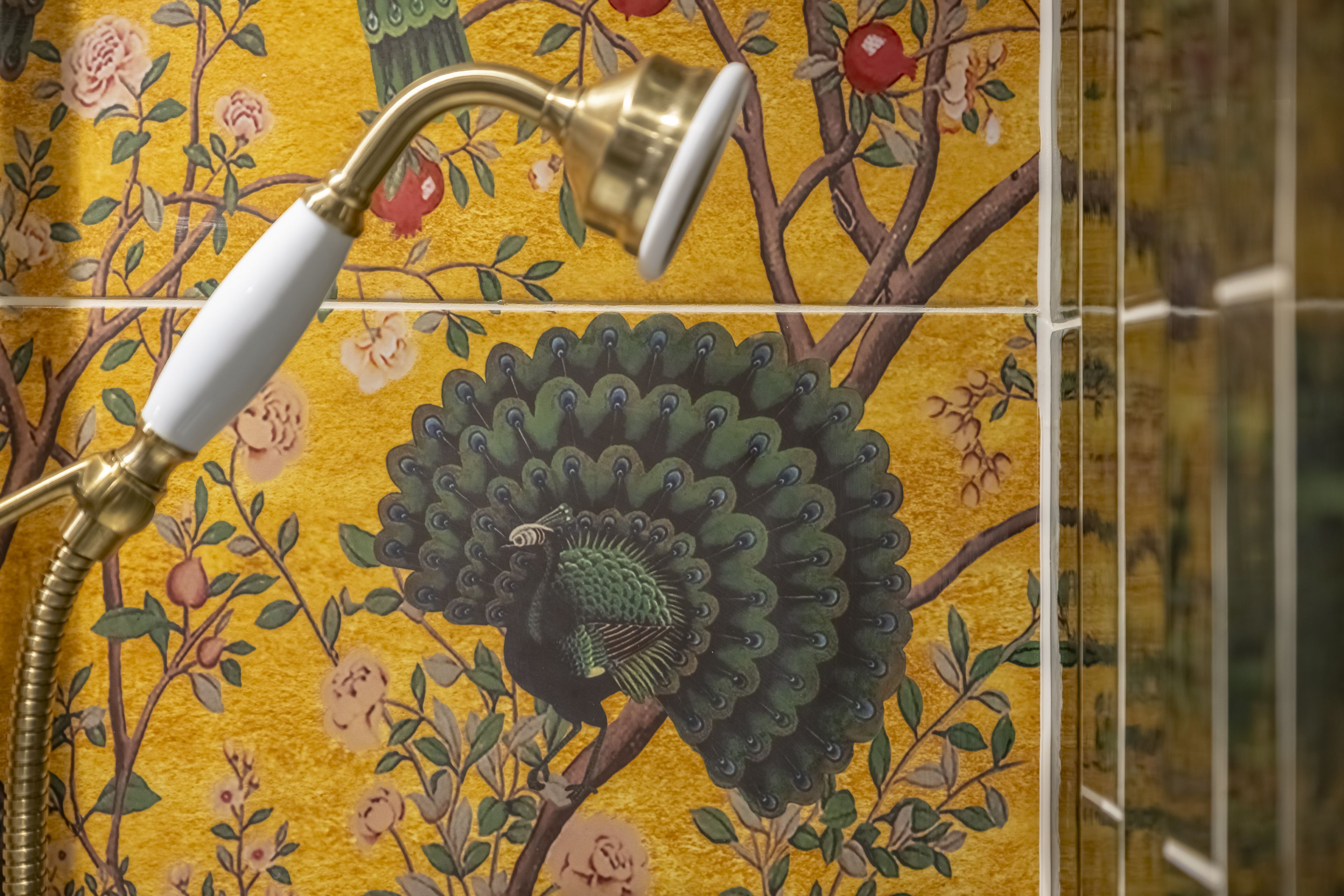 A shower with a brass fixture and a floral tile design.