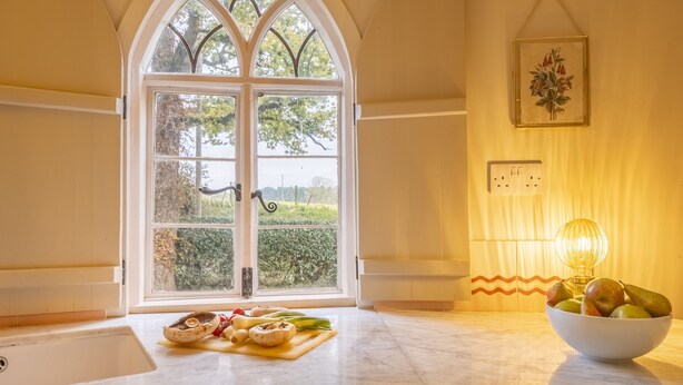 A kitchen with a large window, a bowl of fruit, and a cutting board with vegetables. - A fairy-tale luxurious cottage - The Tea Caddy (Colchester)