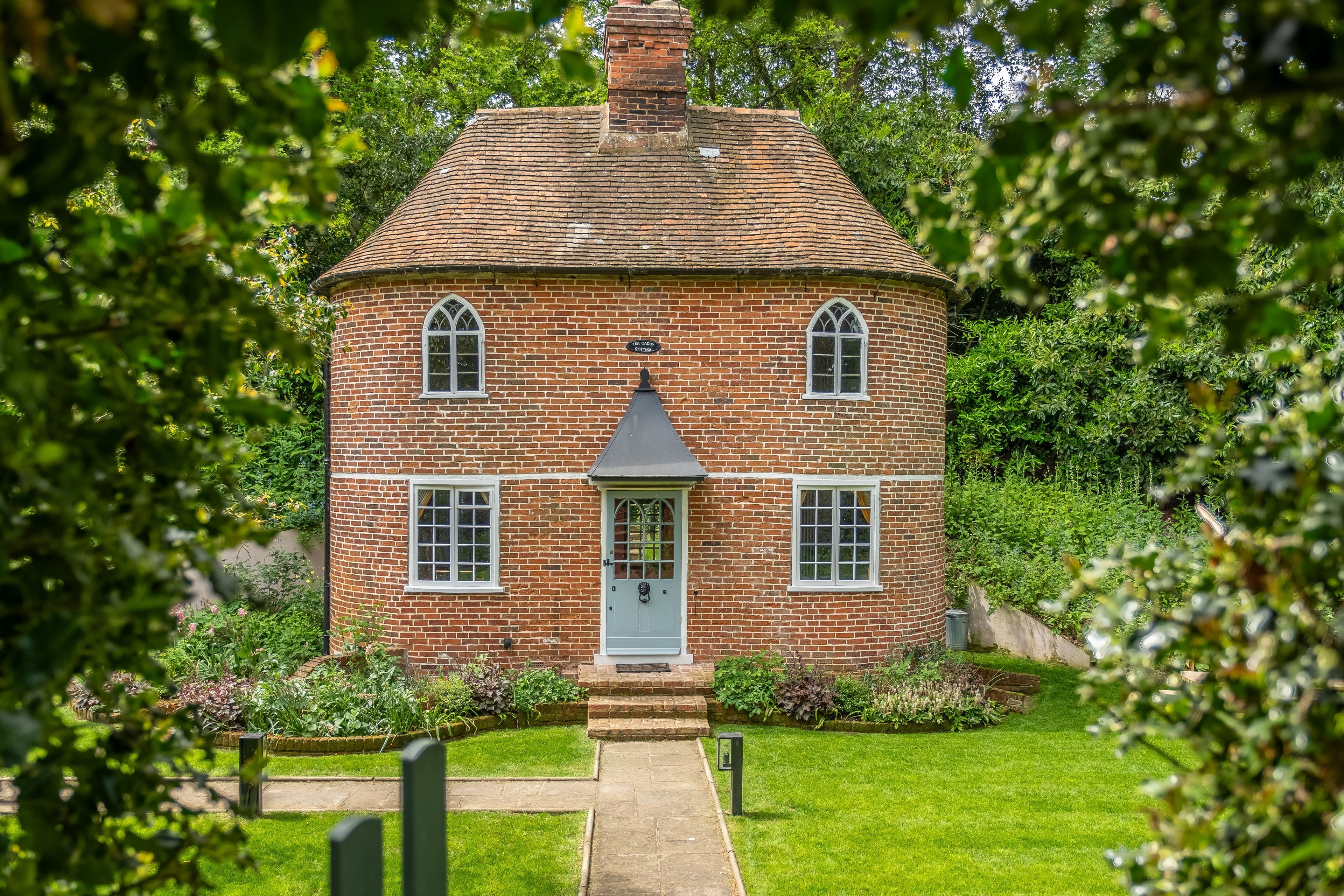 Une maison en briques avec une porte centrale, deux fenêtres de chaque côté et un petit porche.