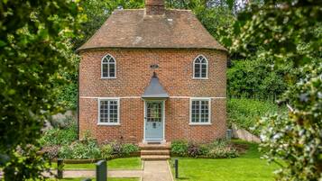 Une maison en briques avec une porte centrale, deux fenêtres de chaque côté et un petit porche.