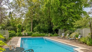 A rectangular swimming pool with a tiled edge, surrounded by a patio area with lounge chairs and a small table. - Barn conversion with private pool - Yew Tree Barn (Colchester)