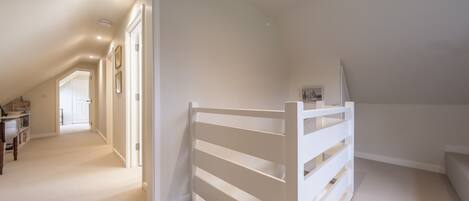 Un espacioso dormitorio en el ático con techo inclinado, estructura de cama blanca y vista al pasillo.