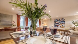 A dining area with a table set for four, featuring white plates, cutlery, and wine glasses. A large vase with flowers is placed in the center. - Barn conversion with private pool - Yew Tree Barn (Colchester)