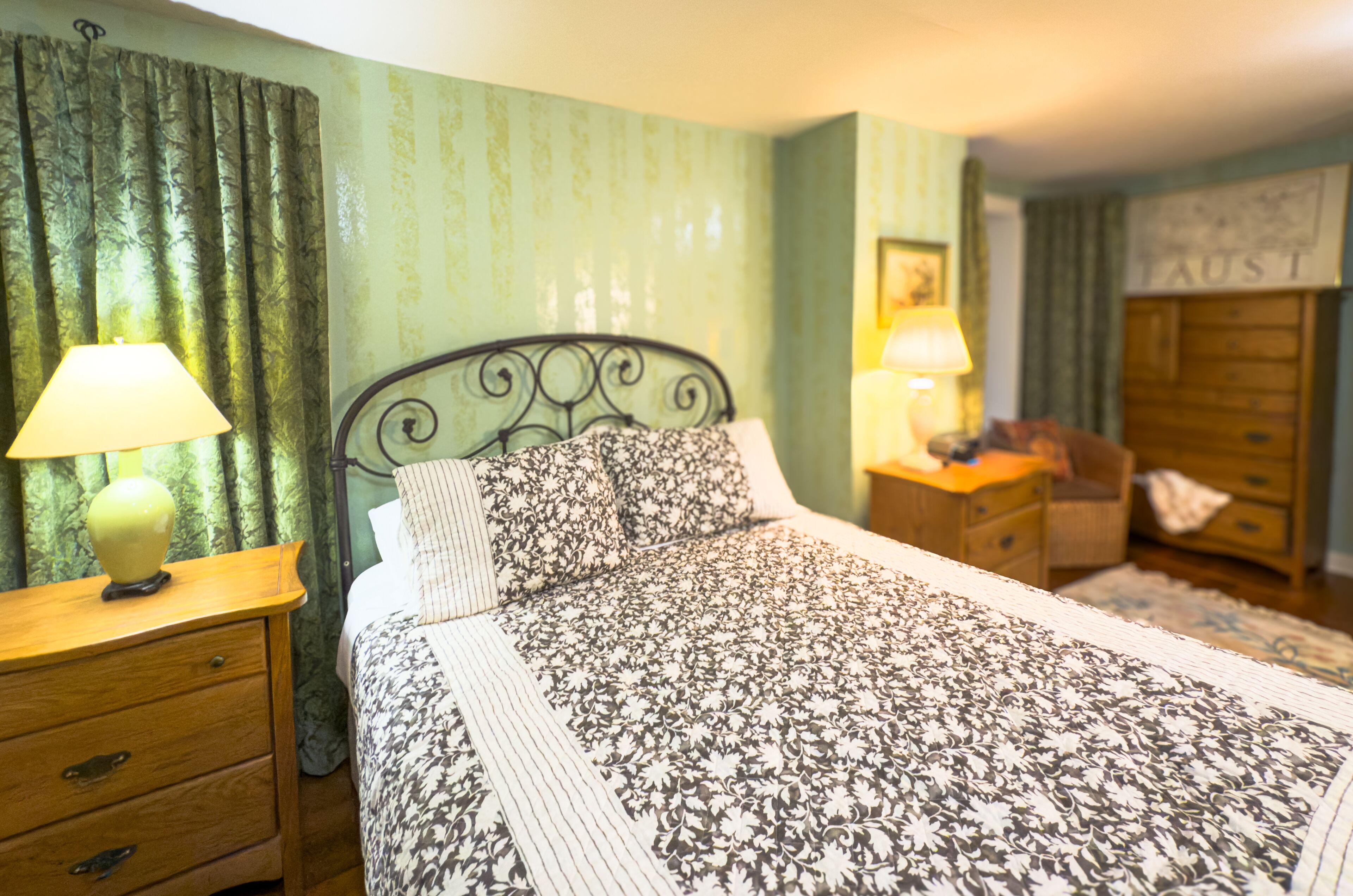 A bedroom with a bed, two bedside tables with lamps, a dresser, and a wall with a sign.