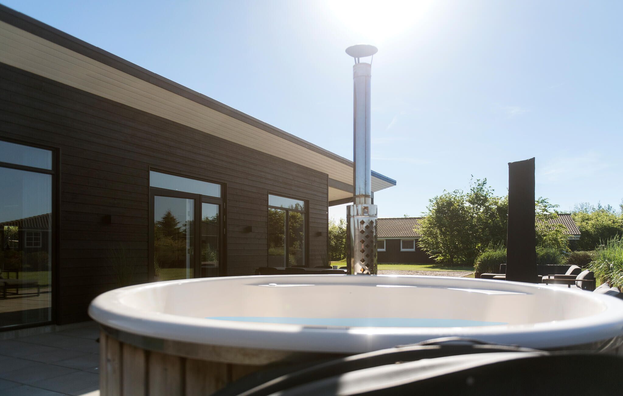Een modern huis met een grote glazen deur en ramen, een houten terras en een jacuzzi.