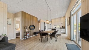 A modern kitchen with a central island, wooden panel walls, and a dining area with a large table and chairs. - Pet friendly home in Hemmet with WiFi (Hemmet)