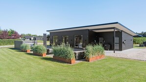 A modern two-story building with a covered patio area, large windows, and a well-maintained lawn with decorative plants. - Pet friendly home in Hemmet with WiFi (Hemmet)