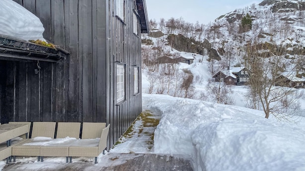 A wooden building with a balcony and outdoor seating area, surrounded by snow-covered landscape and mountains. - Stunning home in åseral with sauna (Åseral)