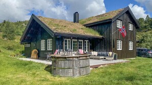 A wooden cabin with a thatched roof, a deck with outdoor furniture, and a flag. - Stunning home in åseral with sauna (Åseral)