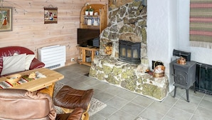 A cozy living room with a stone fireplace, a wooden sofa, a table with a bowl, and a television. - Stunning home in åseral with sauna (Åseral)