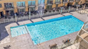 Une piscine rectangulaire avec une terrasse carrelée, entourée d’une rambarde en métal.