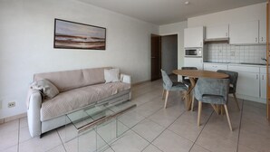 Un salon moderne avec un canapé, une table basse en verre et un coin repas comprenant des chaises et une table en bois.