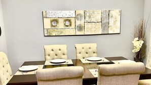A dining area with a rectangular table, four upholstered chairs, and a decorative wall piece above the table. - Comfortable and family-friendly 3BR House in Cranston w/ AC (Calgary)