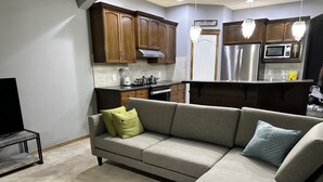 A modern kitchen with wooden cabinets, stainless steel appliances, and a grey sofa with cushions. - Comfortable and family-friendly 3BR House in Cranston w/ AC (Calgary)