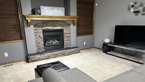 A living room with a stone fireplace, a mounted television, and a sofa with a throw pillow. - Comfortable and family-friendly 3BR House in Cranston w/ AC (Calgary)