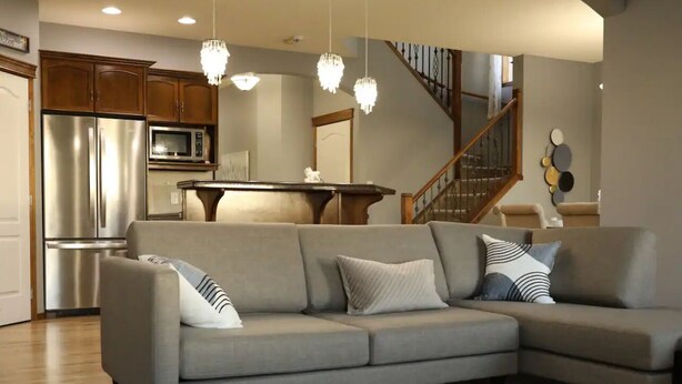 A modern living room with a sectional sofa, a dining table, and a kitchen area with stainless steel appliances. - Comfortable and family-friendly 3BR House in Cranston w/ AC (Calgary)