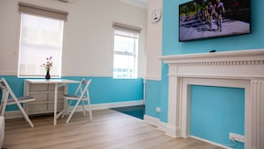 A room with a television displaying a cycling event, a white fireplace, and a table with chairs. - Lovely Studio Apartment in Downtown Albany (Albany)