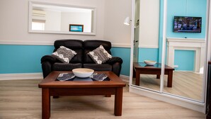 A living room with a black leather sofa, a wooden coffee table, and a small side table. - Lovely Studio Apartment in Downtown Albany (Albany)