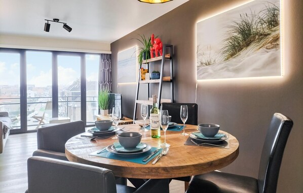 A dining area with a round wooden table set for four, surrounded by modern chairs. A wine bottle and glasses are on the table, and a bookshelf with decorative items is in the background. - Cozy apartment in Oostende with WiFi (Oostende)