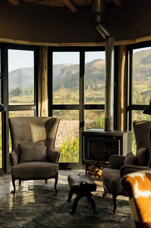 A cozy room with a large fireplace, wicker chairs, and a view of the mountains. - PUQIO by Andean (Yanque)