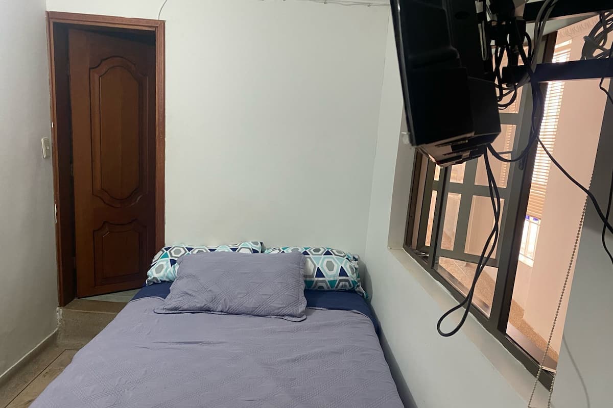 A bedroom with a bed, a wooden door, and a window with blinds.