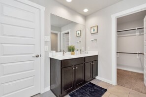 A modern bathroom with a white door, dark cabinets, a large mirror, and a walk-in closet. - Rammies 3 bedroom Home W/Pool Access (Fulshear)