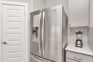 A stainless steel refrigerator with a water and ice dispenser, a blender on a countertop, and a white door with a handle.
