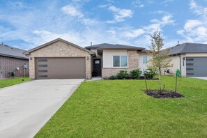 A residential house with a garage, a small front yard with a tree, and a clear sky. - Rammies 3 bedroom Home W/Pool Access (Fulshear)