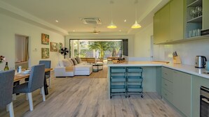 A modern kitchen with a central island, dining area with a sofa, and a view of the outdoors. - Wake Up to Wonder: Luxurious 4-BR Villa & Majestic Views (Tambon Rawai)