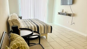 Une chambre d’hôtel avec un lit, une petite table, une chaise, un téléviseur fixé au mur et une fenêtre avec des stores.