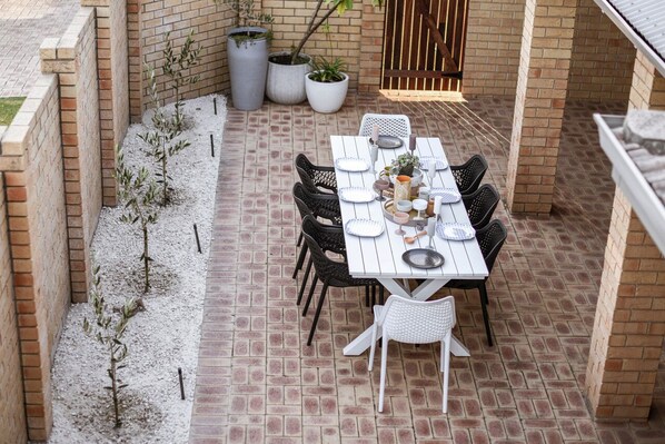 A patio with a brick floor, white table set with plates, cups, and cutlery, surrounded by chairs. - Stylish home to accommodate everyone. Only minutes away from town centre. (Esperance)